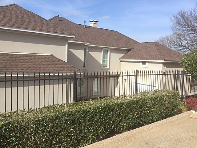 A stucco home with a finished roof behind an iron fence